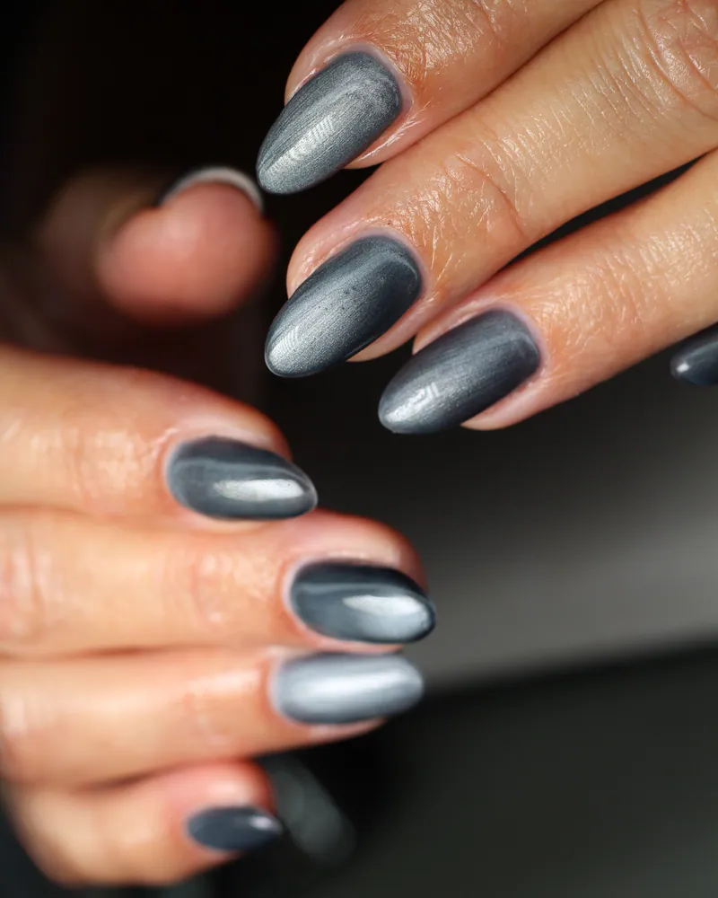 Two hands with almond nails in a deep grey magnetic cat-eye finish, a soft silver line of light down the middle of each nail.