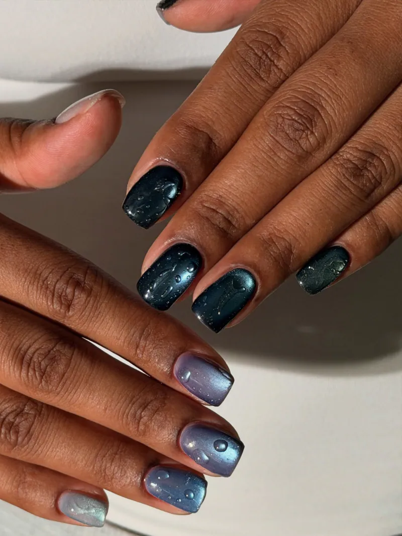 Kazani’s hands with short square nails in dark teal and blue-lilac magnetic finishes under a glossy top coat.