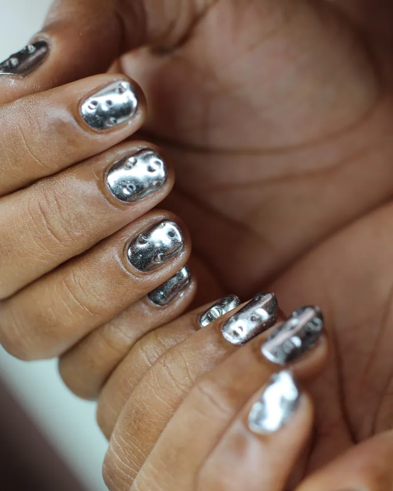 A hand with short nails finished in rippled, mirror-bright silver chrome.