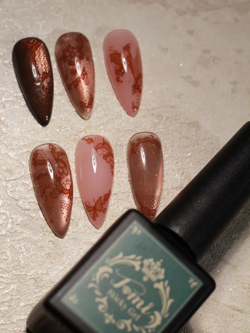 Stiletto sample tips with brown lace-foil patterns over copper chrome and sheer nude, beside a gel bottle.