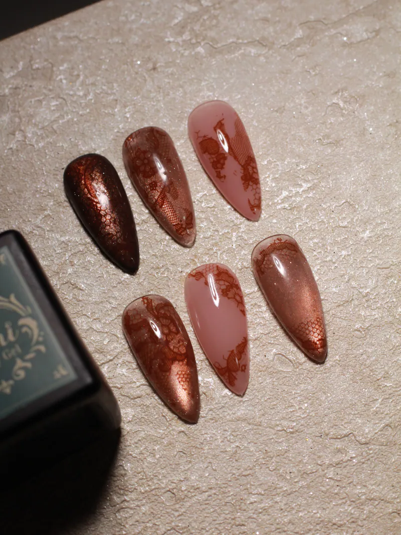 Stiletto sample tips on textured stone: copper chrome and sheer nude tips with brown lace-foil patterns.