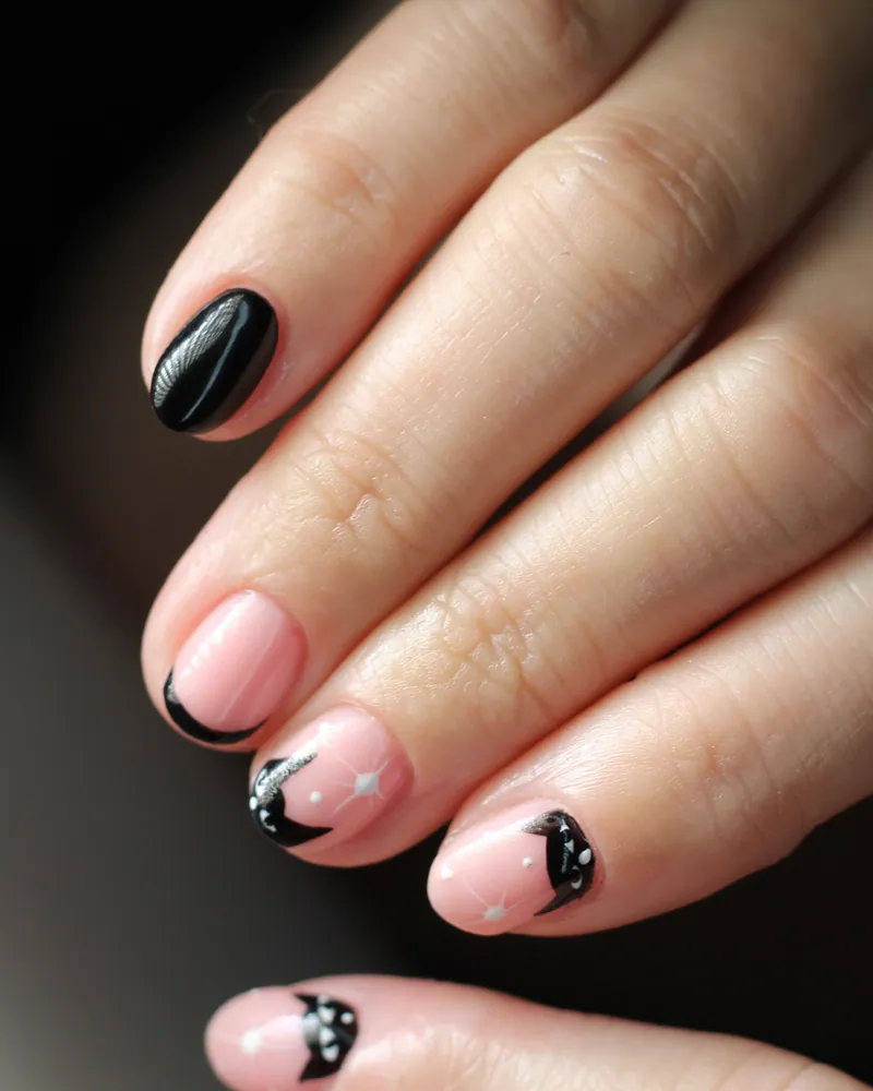 Short rounded nails in sheer soft pink, with small black crescent and dot details near the cuticle on a few nails.