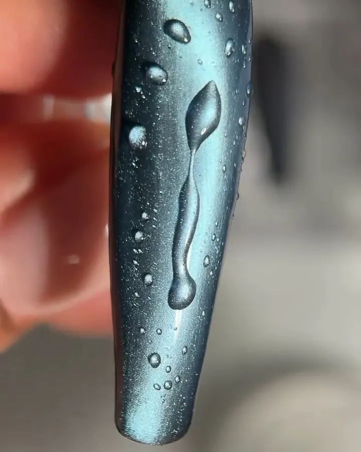 a long silver-blue cat-eye sample tip covered in raised clear droplets; a small magnet moves beside it and the shimmer line shifts.