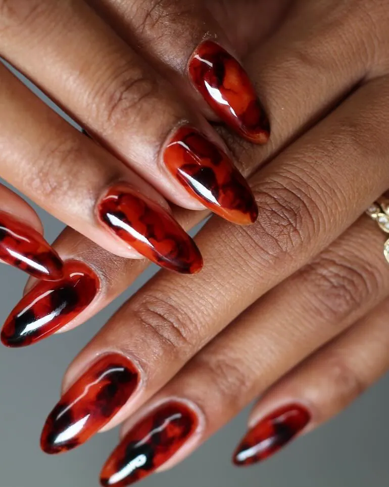 Two hands with almond nails in translucent ruby-red and dark brown tortoiseshell.